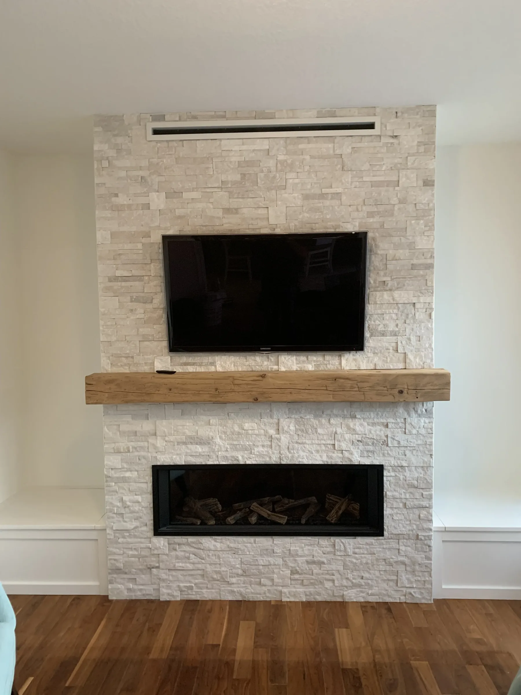 White stacked-stone fireplace with reclaimed wood mantel, twin insets, and TV niche